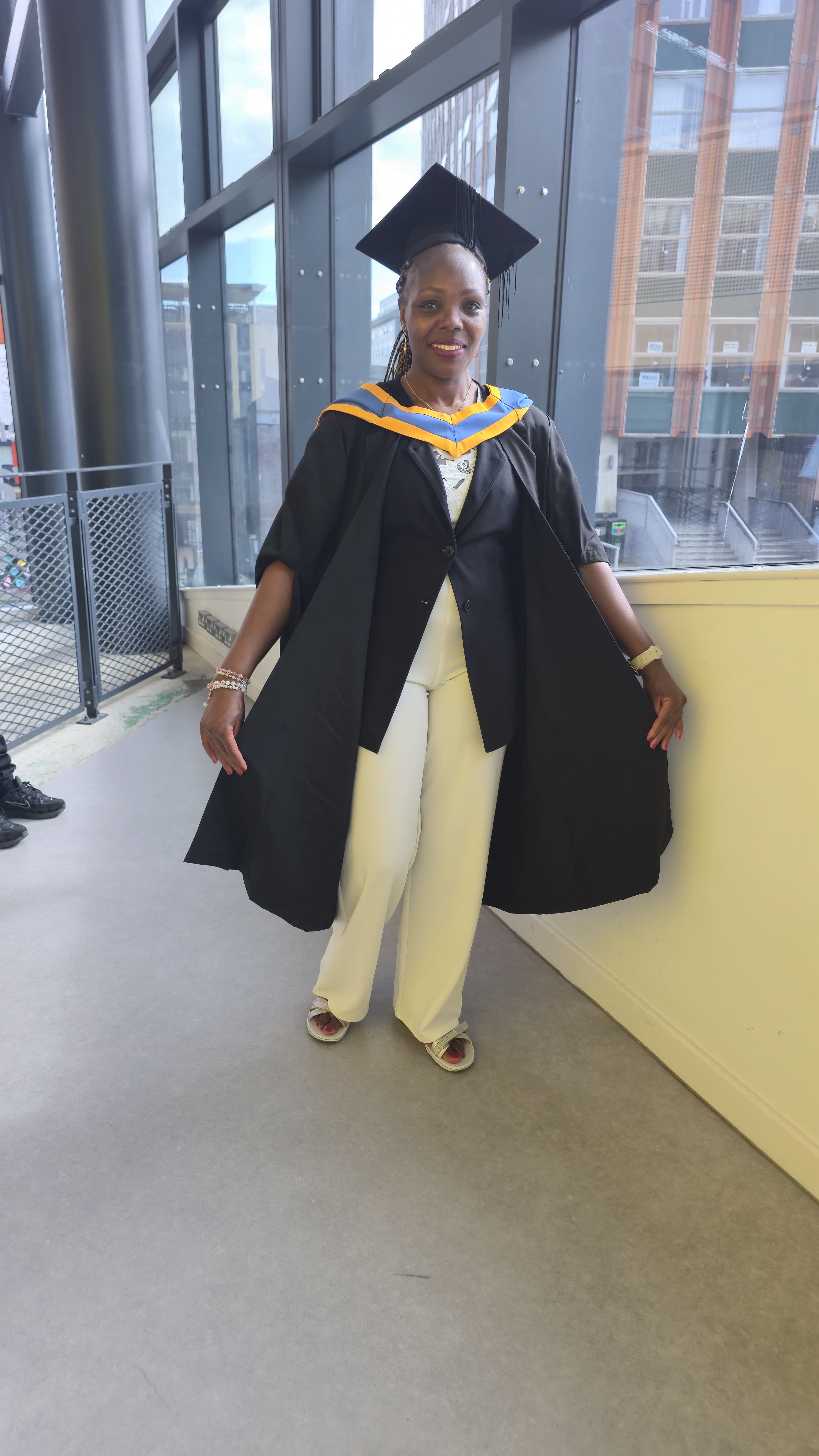 Catherine Cherotich smiling in her graduation gown inside the University of Strathclyde Learning and Teaching Building